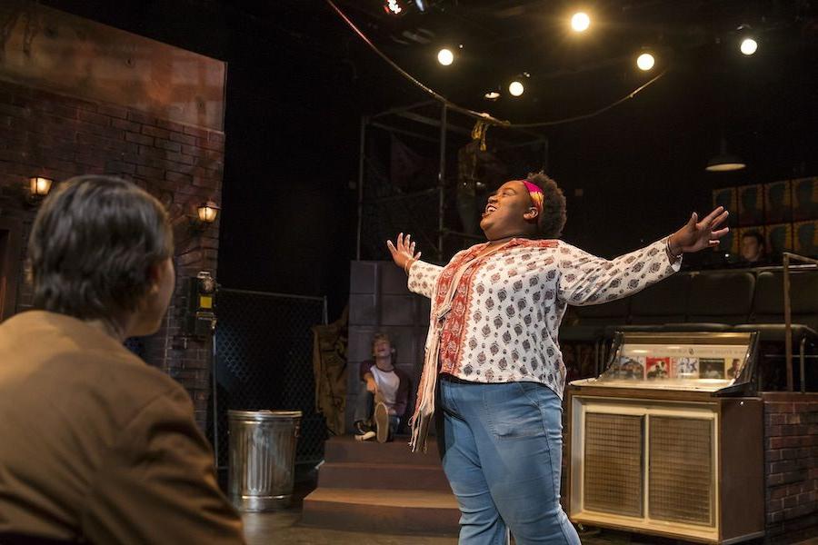 Women with arms outstretched sings on stage.